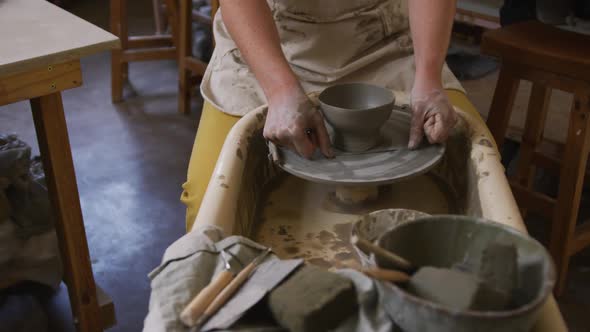 Mid section of female potter using loop tool for finishing pottery at pottery studio