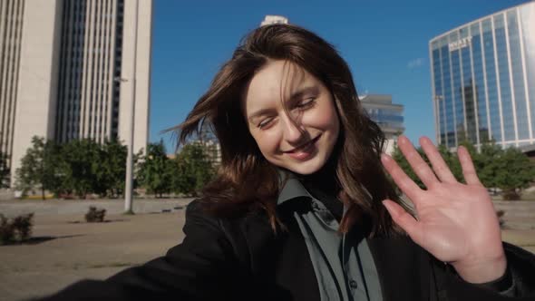 Cute Girl Films Herself and Waves To the Camera Cityscape in the Background