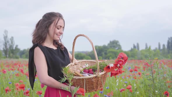 Portrait of Pretty Young Girl Standing in Poppy Field Holding Wicker Basket with Paint, Strawberry