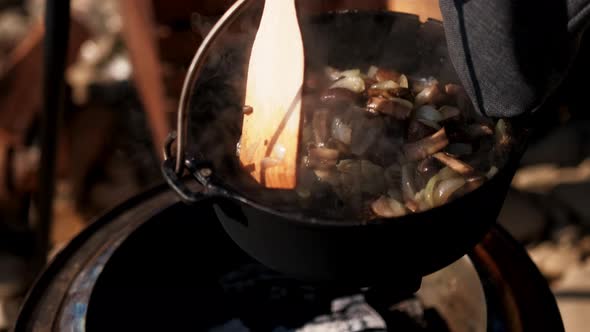 Mushrooms and Onions are Fried in a Pan Over a Fire in the Field