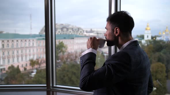 Businessman Drinking Coffee Standing By Window
