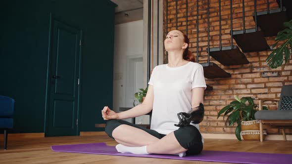 Modern Girl with a Bionic Arm Prosthesis Meditates While Sitting in the Lotus Position on a Yoga Mat