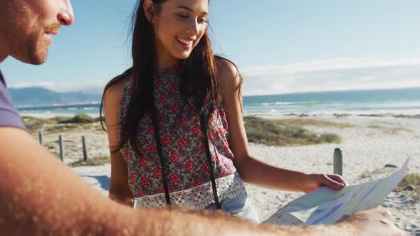 Caucasian couple standing on beach by the sea reading a map