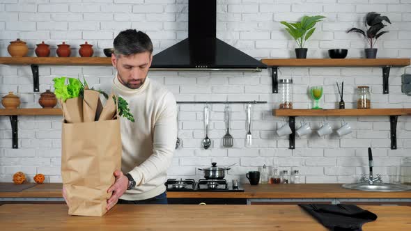 Serious man chef comes to home kitchen puts paper bag with ingredients on table