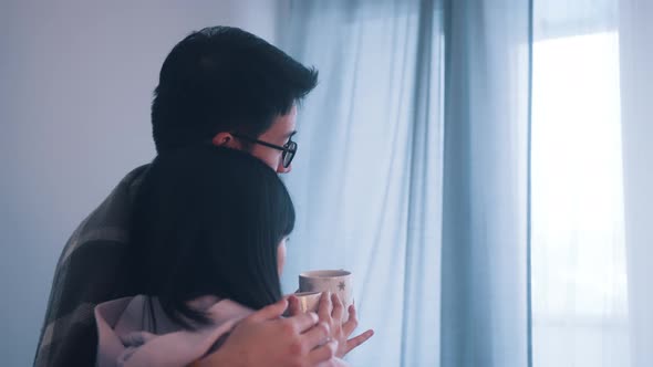 Young Couple Hugging Near the Window with Hot Tea on Stormy Day