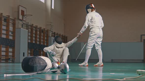 Two Young Women Fencers Having a Training in the Gym - Giving a Hand To Help To Stand Up