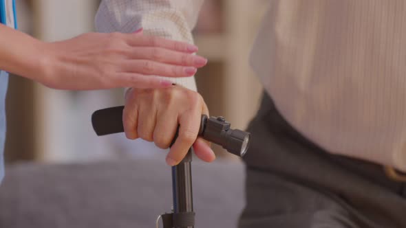 close up hand of doctor or nurse holding hand of elderly patient on cane or walking stick hope and e