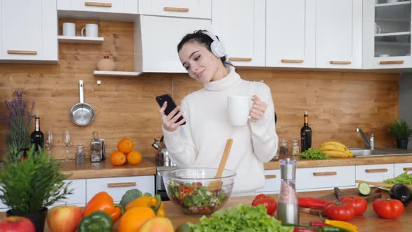 People And Technology Concept, Woman Dancing In Kitchen While Using Smartphone