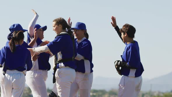 Happy diverse team of female baseball players celebrating after game, smiling and high fiving