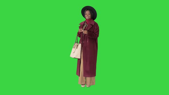 African American Fashion Girl in Coat and Black Hat Posing with a Handbag on a Green Screen, Chroma