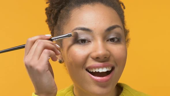 Young Female Applying Eyeshadow Brush on Yellow Background, Beauty Tips, Visage