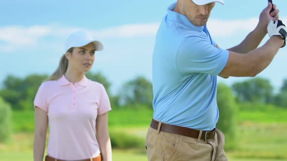 Woman Golf Beginner Player Admiring Man Professionally Hitting Ball, Half-Swing