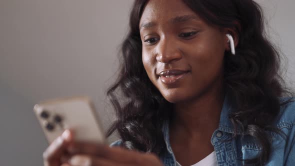 Happy African woman wearing earbuds texting on phone