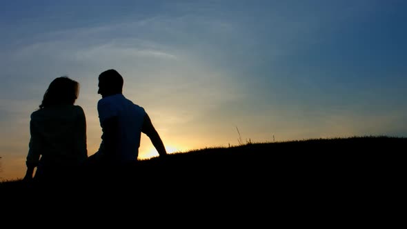 In Love Couple Sitting on a Sunset Background