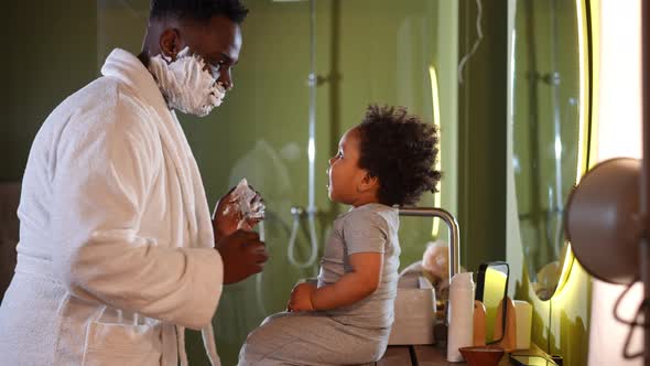 Side View Cute Little African American Boy Sitting in Bathroom with Father Shaving Playing with