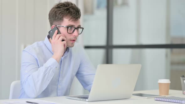 Young Man with Laptop Talking on Phone