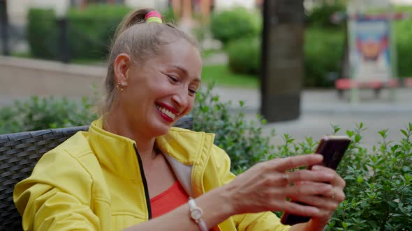 Happy Woman with Mobile Phone in Hands is Resting Alone in Cafe in Downtown