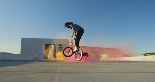 BMX rider on a rooftop jumping and using smoke grenades