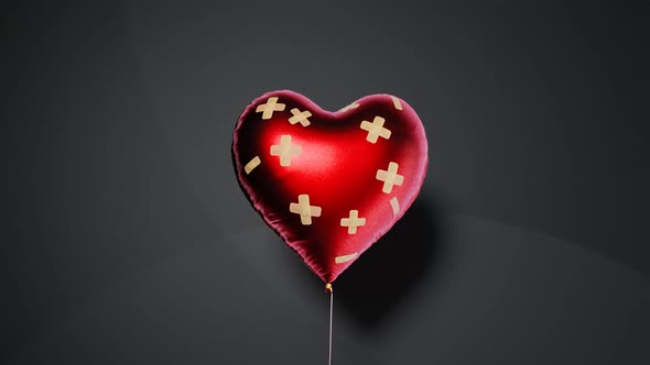 Red heart-shaped balloon fixed with bandaids. Broken heart concept. 4kHD