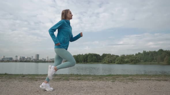 Slow Motion Young Sportswoman in Sportswear Trains in a Park Near the River