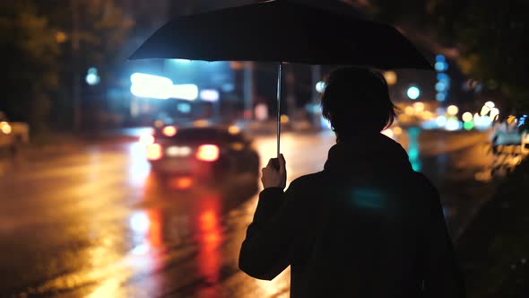 The Man Stands with an Umbrella Against the Background of the Cityscape After the Rain