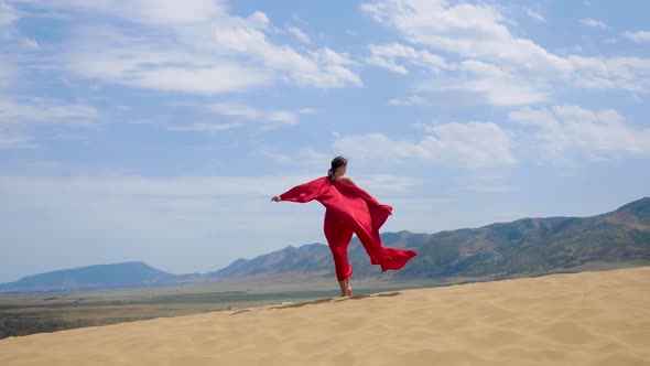 Sexy Brunette Woman in a Red Satin Long Dress Walks on Sand Dunes in the Desert