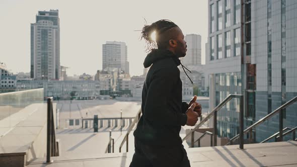 Follow Shot of Sportive African American Man Wearing Sportswear Running in Urban Business Area in