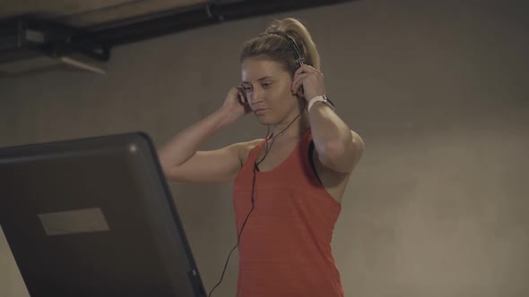 Confident Attractive Woman Putting on Headphones and Adjusting Speed on Treadmill. Portrait of