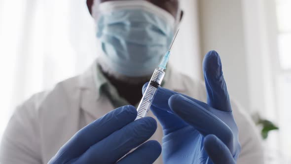 Male african american doctor wearing face mask tapping bubbles out of the syringe