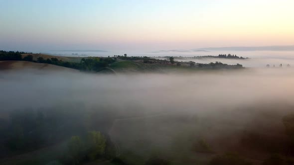Farm fields in Toscany Italy on a foggy morning during sunrise, Aerial slow lowering shot
