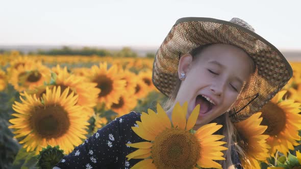 A Happy Little Girl in the Hat Is Smiling at the Field of Sunflowers at Sunset Time