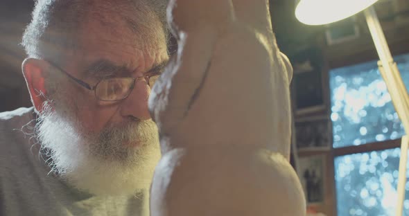 Close up of an old sculptor working on a clay sculpture in his small studio