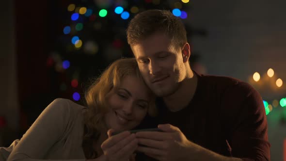 Nice Couple Watching Movie on Smartphone Under Sparkling X-Mas Tree, Intimacy