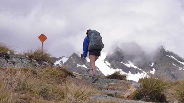 Slider, hiker climbs rocky alpine terrain, distant snow-capped mountains, Routeburn Track New Zealan