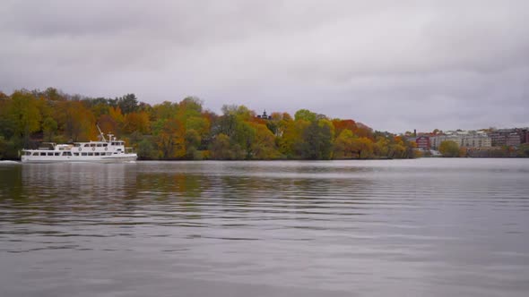 a white small ferry is going from one island to another in Stockholm in the autumn with colorful tre