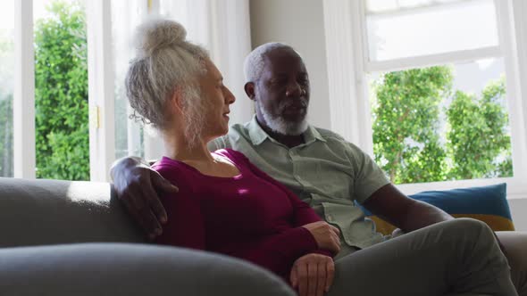 Mixed race senior couple taking to each other while sitting on the couch at home