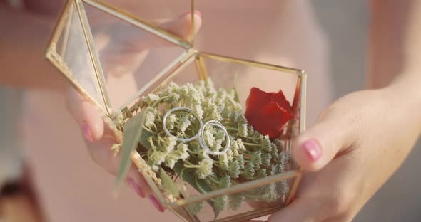 Women's hands hold a box with wedding rings and flowers