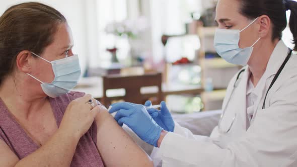 Caucasian woman and female doctor wearing face masks, vaccinating