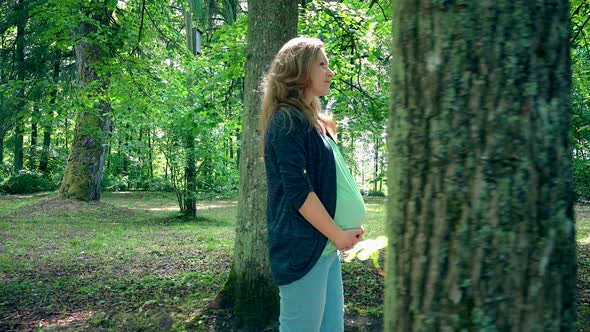 Happy Pregnant Woman in Ninth Month Pregnancy Walk in Park and Smile on Sunlight