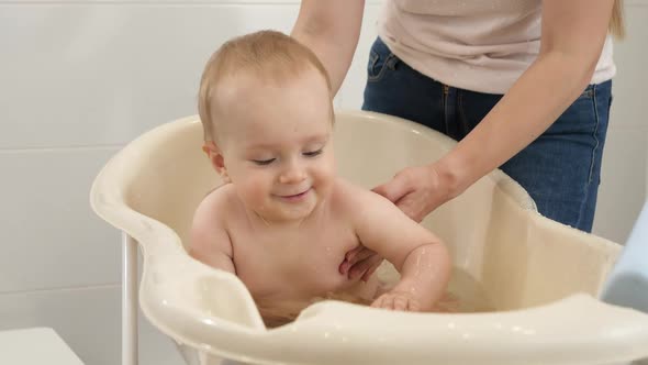 Cheerful Smiling Baby Boy Splashing Water and Playing While Having Bath with Mother