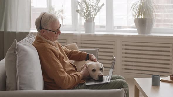 Senior Man with Laptop Petting His Cute Dog