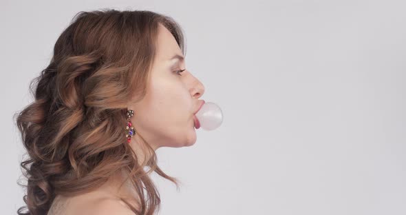 Side View of Young Woman Blowing Pink Bubble Gum