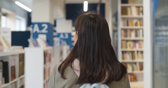 Back View of Teen Girl with Backpack Walking in School Library