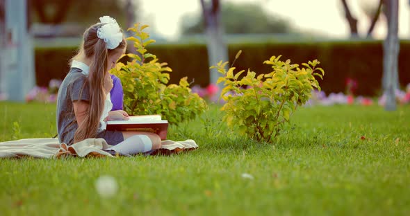 Young Pretty School Girl Reading Book in Park