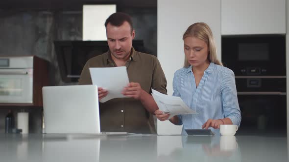 Serious Young Couple Pay Bills Online on Website App Doing Paperwork in Kitchen