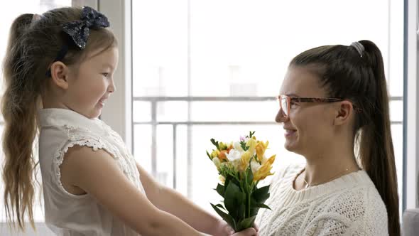 6-7 Year Old Girl Gives a Bouquet of Freesias and Hugs Her Mother. Mom's Birthday or Mother's Day.