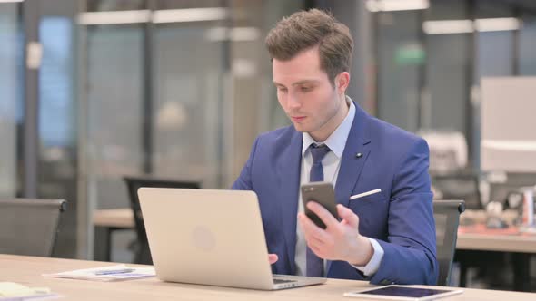 Businessman Using Smartphone While Using Laptop in Office