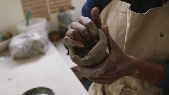 Mid section of female potter wearing apron working on clay to create pot at pottery studio
