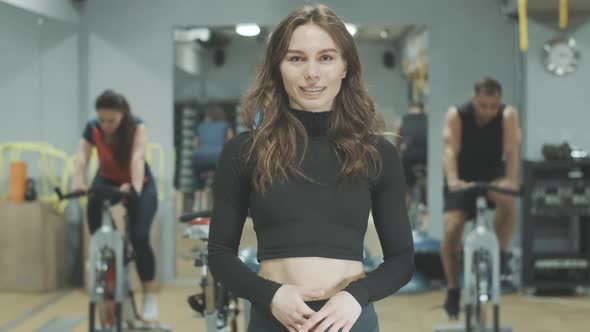 Slim Brunette Beautiful Woman Standing in Gym and Smiling at Camera. Portrait of Young Confident