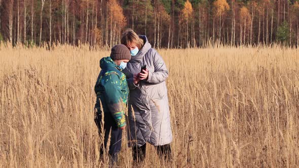 Mom and Son with Masks on Their Faces in the Field Use the Phone